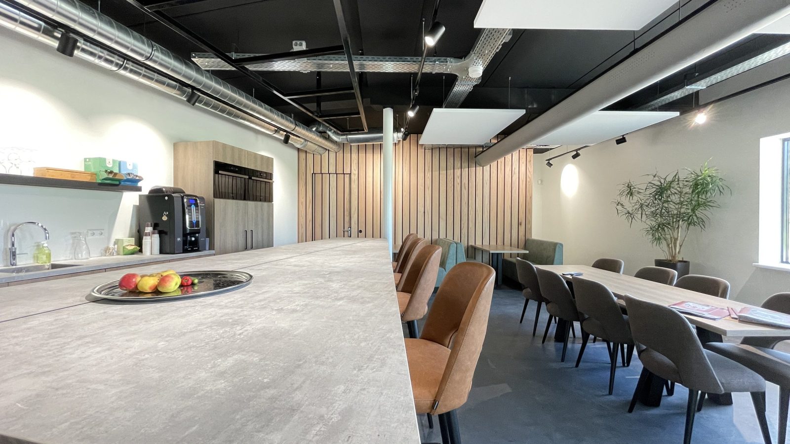 De gedeelde ruimte bij KE Fibertec met een lange lichte bar, bruine barkrukken, grijze stoelen en houten wandbekleding onder een zwart plafond.