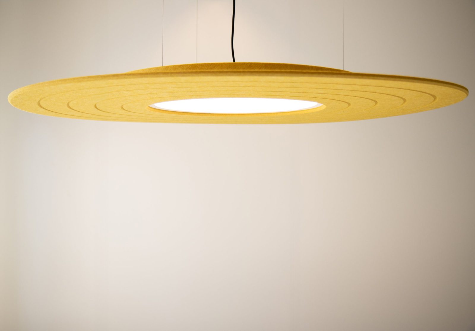 Een gele ronde hanglamp tegen een lichte achtergrond bij AVAS.