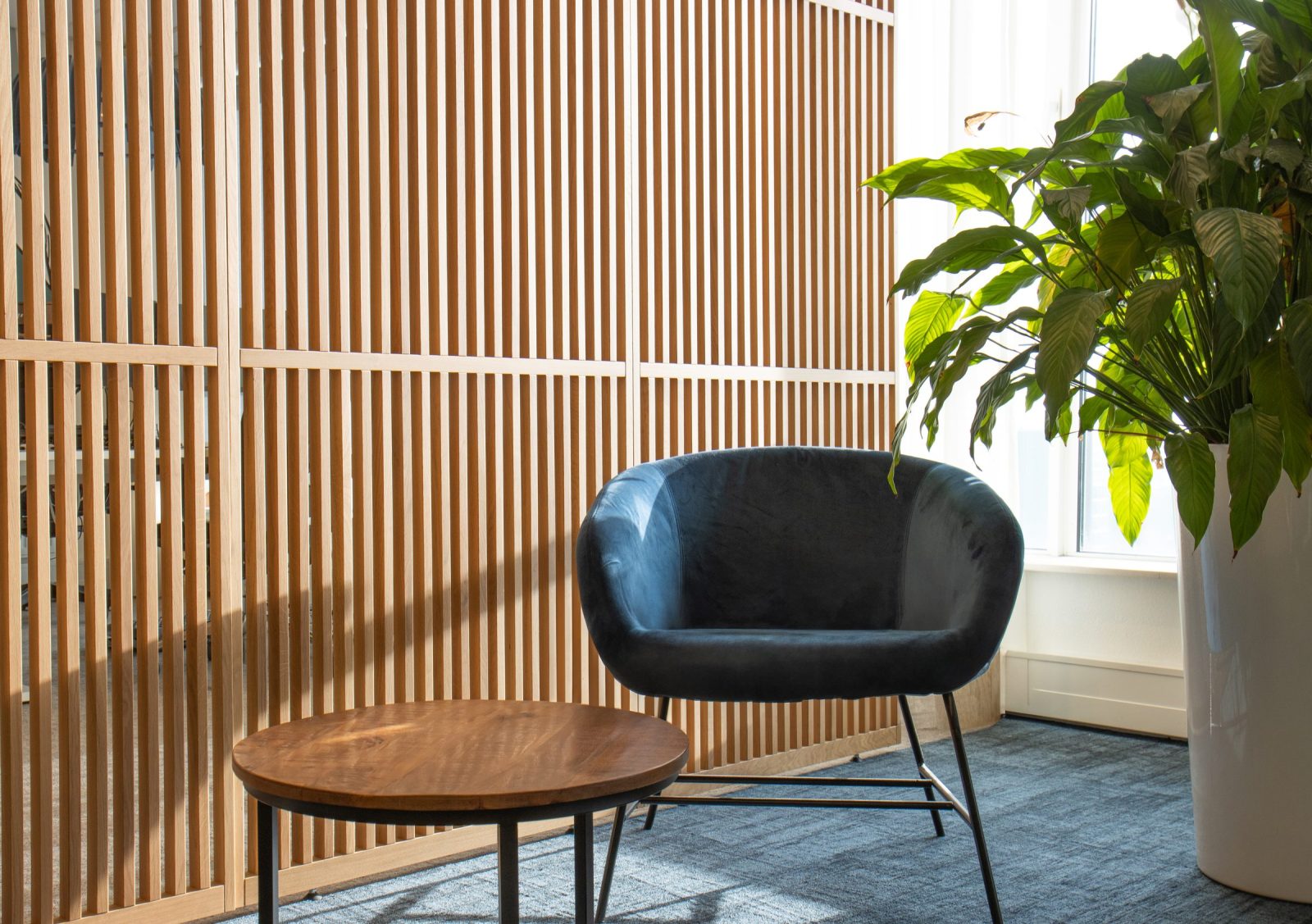 Een donkerblauwe fauteuil naast een houten lattenwand, een ronde tafel en een plant bij Finance.
