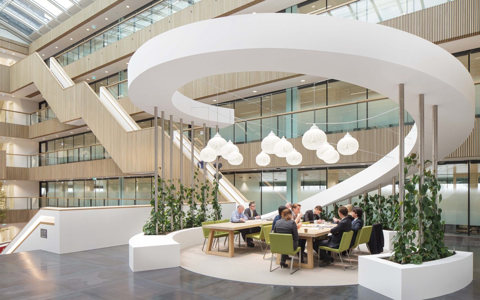 Het atrium van Fluor met een grote witte spiraalvorm, houten wandbekleding en een gedeelde tafel met groene stoelen.