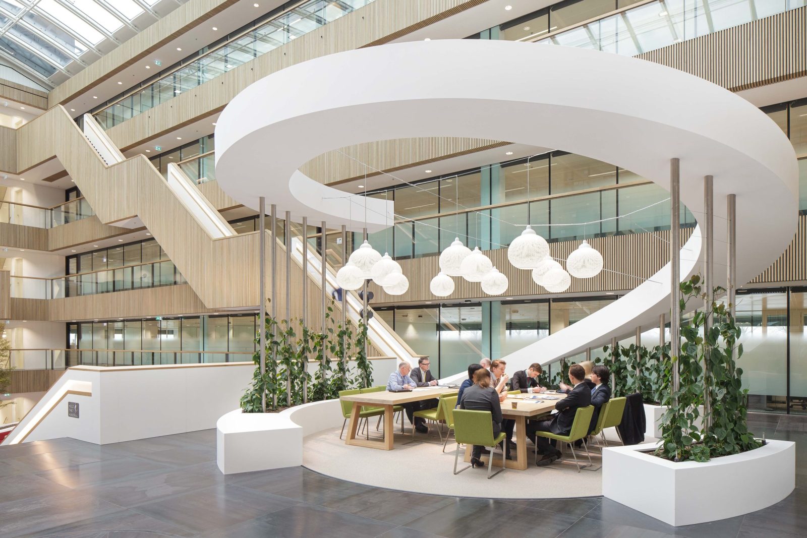 Het Fluor-atrium met een grote witte gebogen vorm boven een zitplek, hanglampen, planten en een glazen dak.