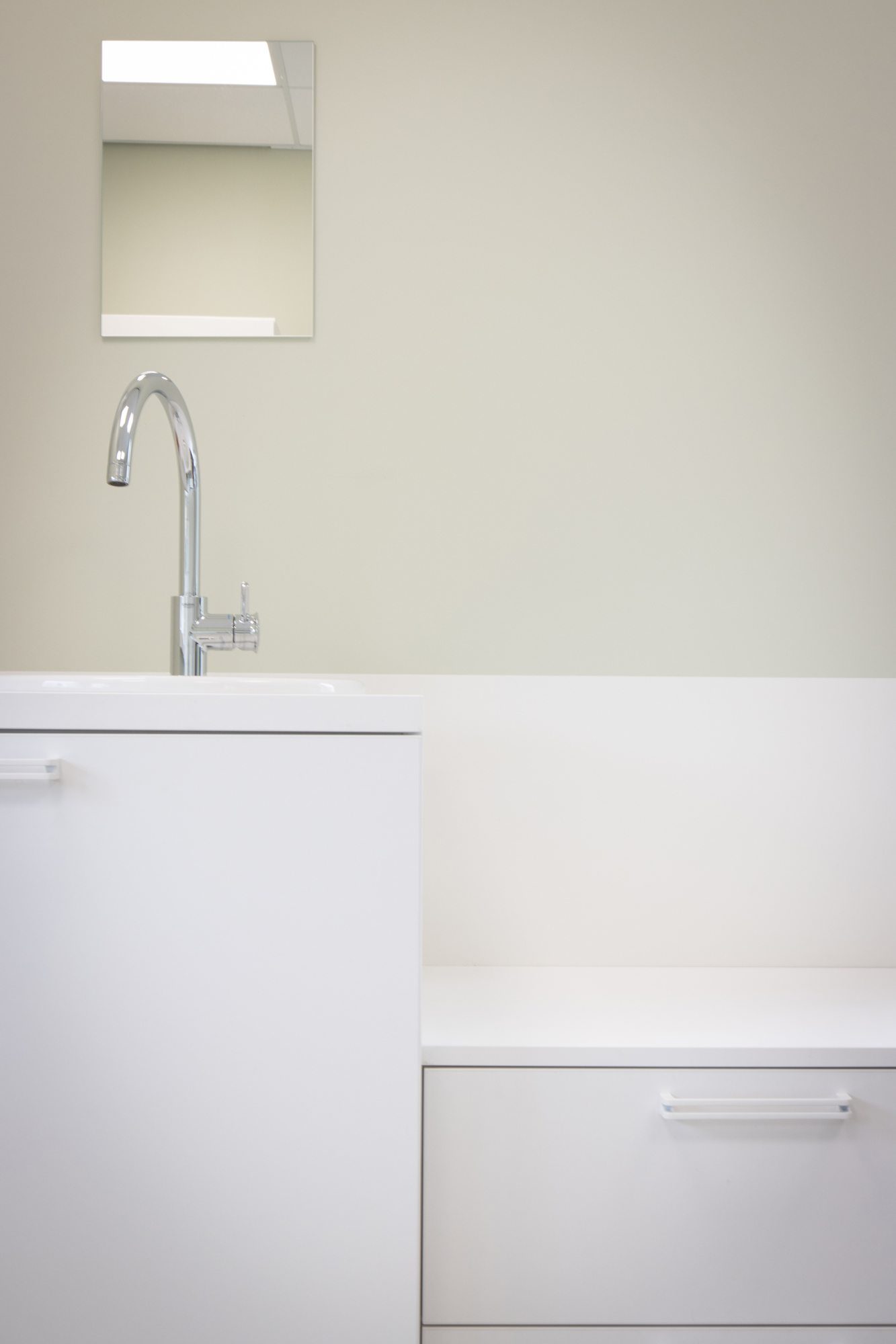 Detail van witte kastfronten en een werkblad naast een grijsgroen wandvlak in een behandelkamer.