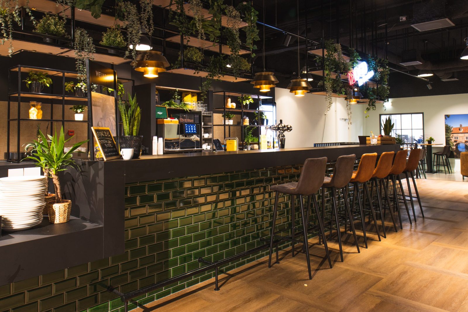 De bar bij OGD Delft met diepgroene tegels, een donker blad, hoge stoelen, hangplanten en houten vloer.