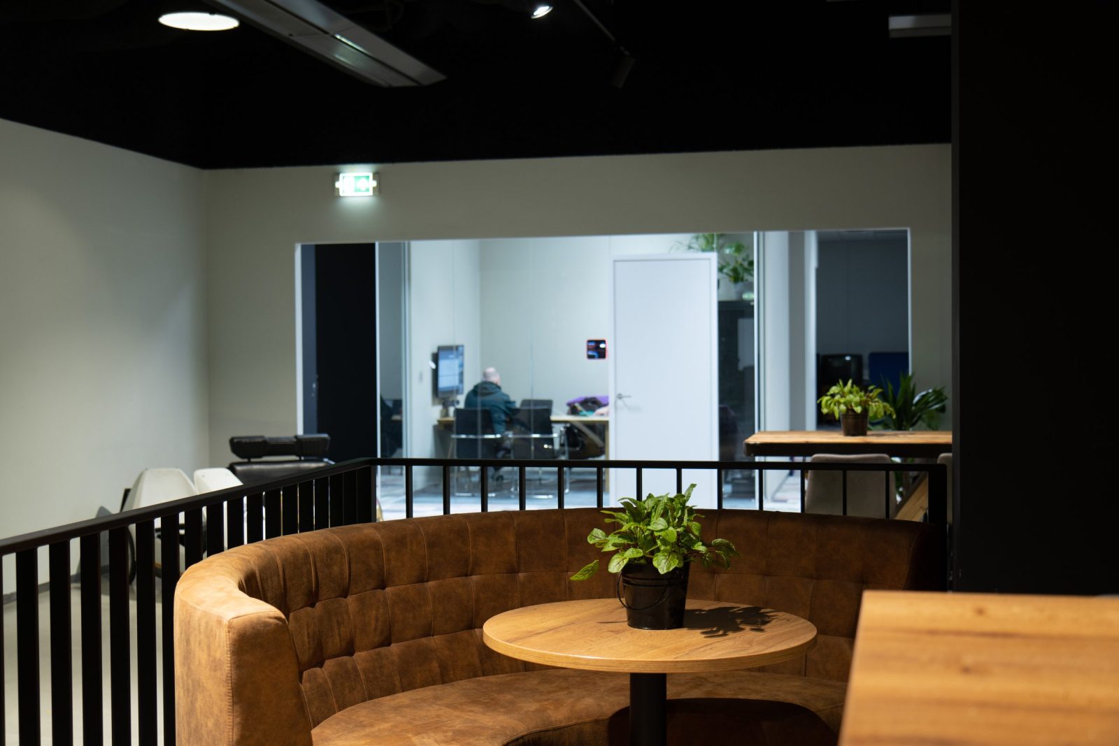 Een gebogen cognackleurige zitbank rond een houten tafel, met glazen vergaderwanden op de achtergrond.