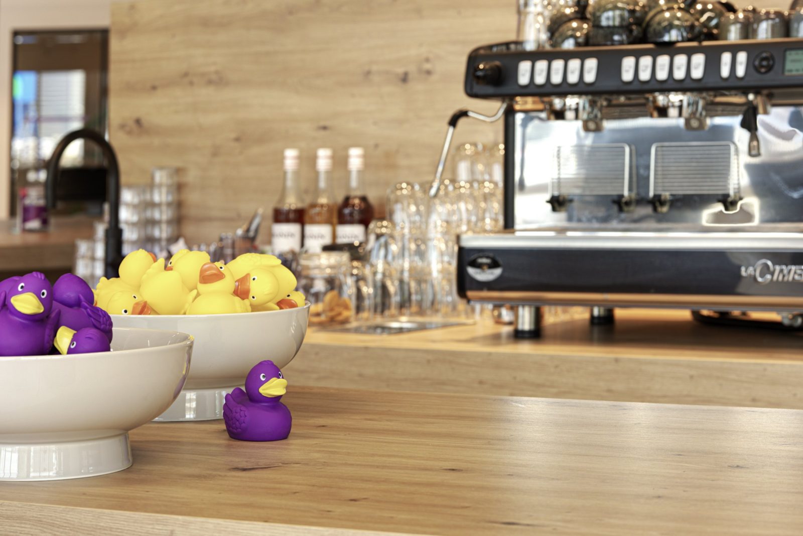 Detail van het houten koffieblad met een espressoapparaat, glazen, flessen en een fruitschaal.