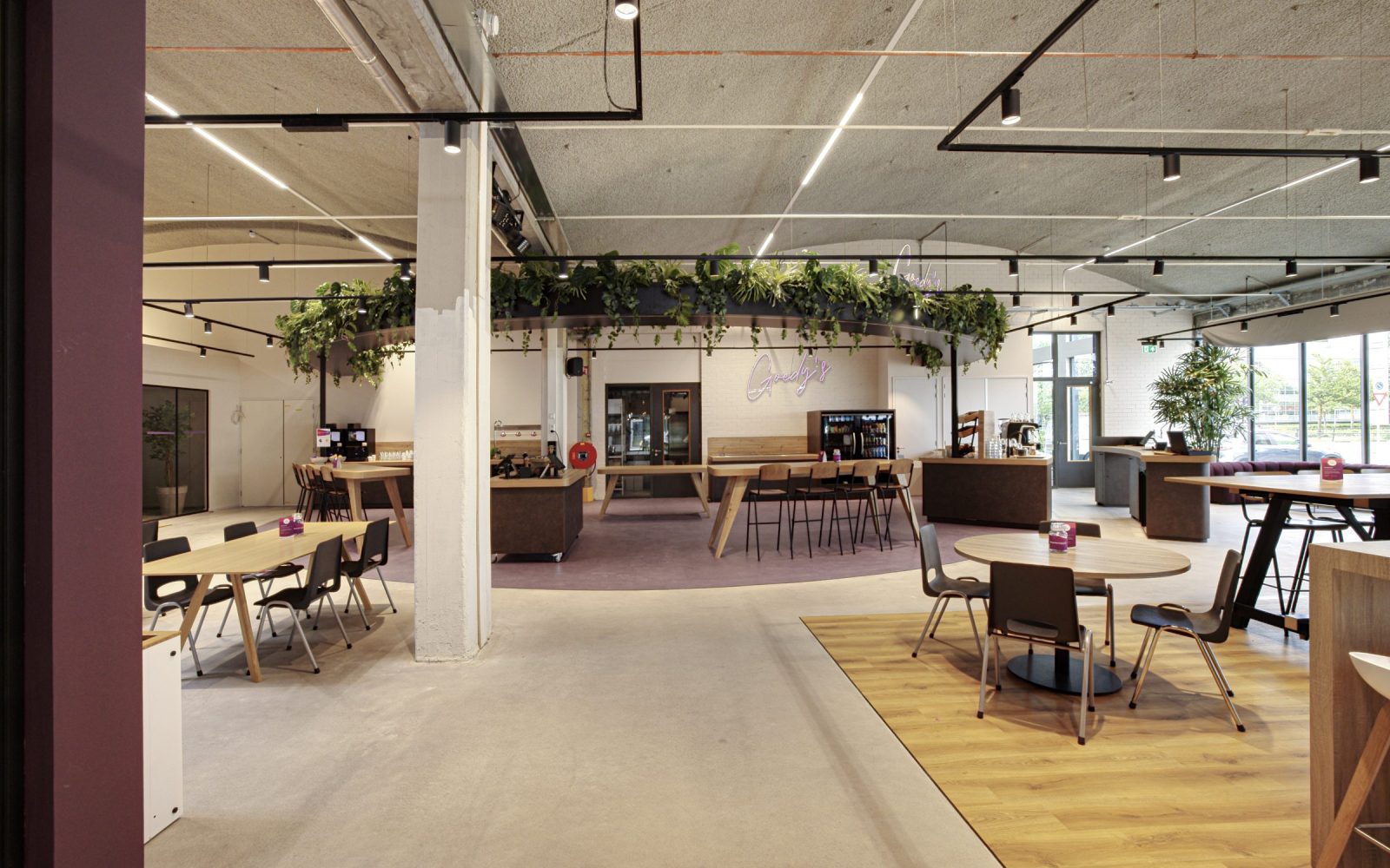 De gezamenlijke ontmoetingsruimte bij Vebego Eindhoven, met houten tafels, zitplekken, planten en een koffiebar.